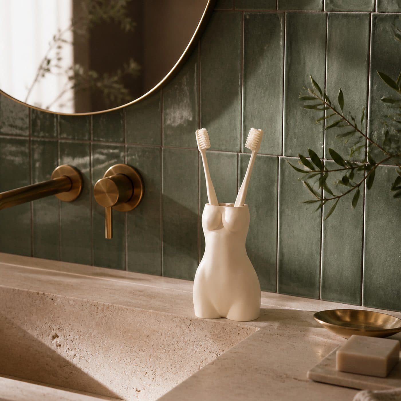 Rangement de salle de bain déco La Favorite blanc sur un plan en travertin, carrelage vert et branche d'olivier